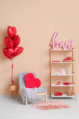 Gri koltuk, kalp şeklinde balonlar ve bej duvarın yanında Sevgililer Günü kutlamaları için dekorasyonlu kitaplık.