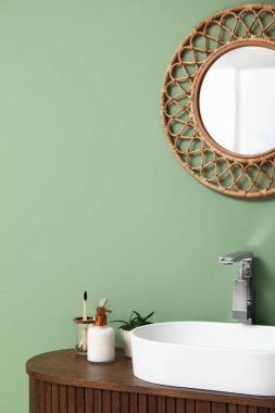 Tezgahta banyo malzemeleri ve banyoda yeşil duvarın yanında şık bir ayna olan modern lavabo.