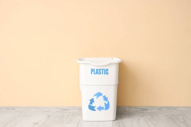 Bej duvarın yanında PLASTIC işareti olan boş çöp kutusu. Geri dönüşüm kavramı