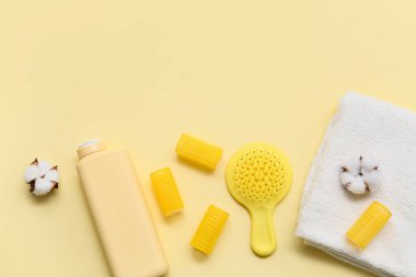 Saç fırçası, bigudiler, bir şişe şampuan ve sarı arka planda pamuk çiçekli havlular.