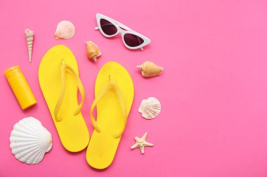 Terlikli kompozisyon, güneş gözlüğü, güneş kremi ve pembe arka planda deniz kabukları.