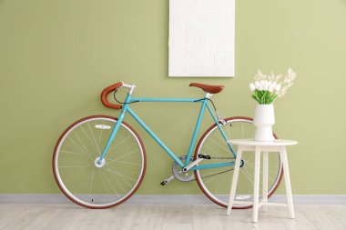 Yeşil duvarın yanındaki vazoda bir buket lale çiçeği ve bisiklet.