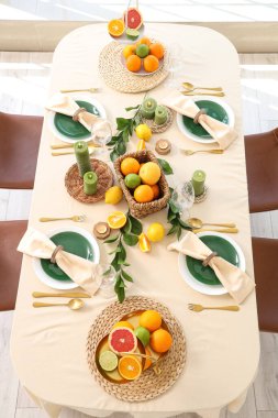 Oturma odasında turunçgiller, yanan mumlar ve yeşil yapraklarla dolu güzel bir masa.