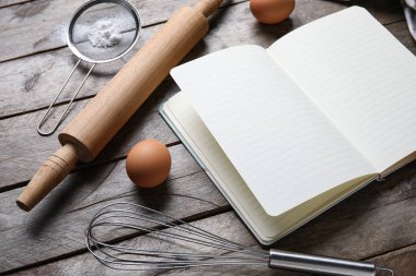 Ahşap zemin üzerinde boş tarif defteri, yumurta ve kap kacak içeren kompozisyon