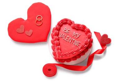 Kalp şeklinde yastıklı tatlı bento pastası ve beyaz arka planda nişan yüzükleri. Sevgililer Günü kutlaması