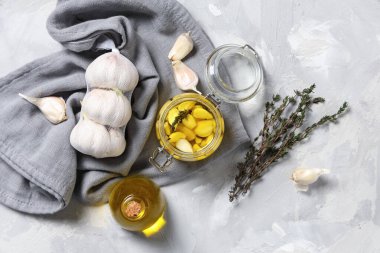 Kavanoz ve bir şişe taze sarımsak yağı ve gri arka planda kekik.