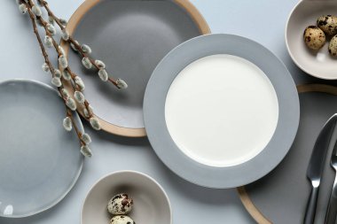 Different clean plates with quail eggs and pussy willow branches on grey background. Easter celebration
