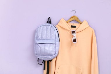 Şık, şeftali rengi kapüşonlu, güneş gözlüklü ve sırt çantalı bir askı.