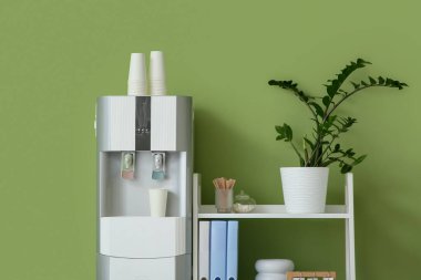 Modern su soğutucusu ve raf ünitesi yeşil duvarın yanında, yakın plan.