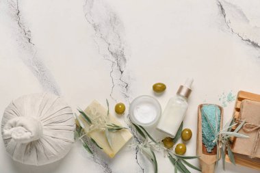 Doğal kozmetik ürünleri, masaj çantası ve hafif arka planda yeşil zeytinli kompozisyon