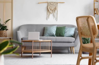 Rahat bir kanepe ve odasının içinde modern dizüstü bilgisayar olan ahşap bir masa.