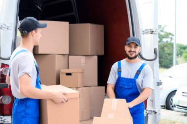 Erkek nakliyeciler açık hava arabasından kutuları boşaltıyor.