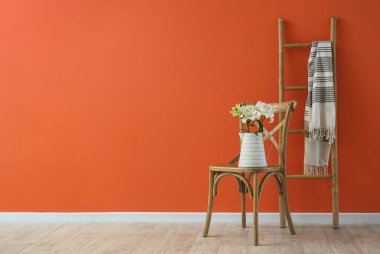 Turuncu duvarın yanındaki sandalyede güzel çiçekli vazo.