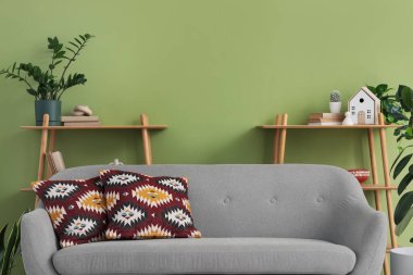 Yeşil duvarın yanında rahat gri kanepesi ve çiçekleri olan şık bir oturma odası.