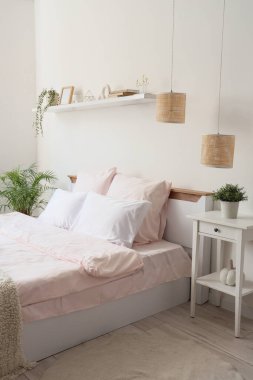 Şık pembe yataklı yatak, komodinli masa, ev bitkileri ve yatak odasındaki raflarda ev dekorasyonu.