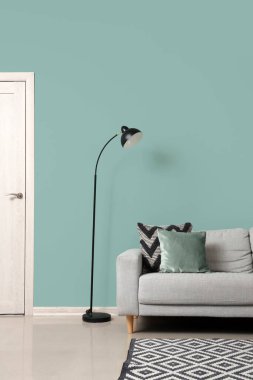 Oturma odasındaki yeşil duvarın yanındaki siyah lamba ve kanepe.
