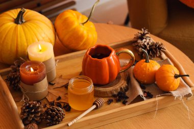 Bir fincan çayla sonbahar kompozisyonu, bal, balkabağı ve masada yanan mumlar.