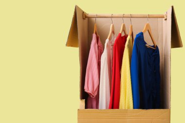 Sarı arka planda giysileri olan gardırop kutusu.