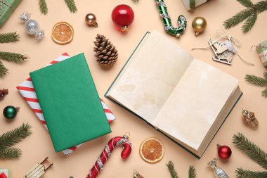 Noel süsleri, kurutulmuş portakal dilimleri ve bej arka planda köknar dalları olan kitaplar.