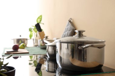 Bej duvarın yanındaki elektrikli ocakta paslanmaz tencereler, yakın plan.