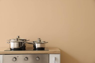 Bej duvarın yanındaki elektrikli ocakta paslanmaz tencereler.