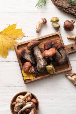 Beyaz ahşap zemin üzerinde taze mantar ve sonbahar yaprakları olan tahta.