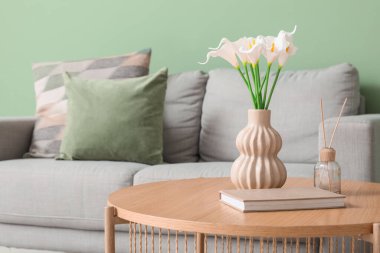 Yapay çiçekli vazo, kitap ve kamış ayırıcı oturma odasındaki masada.