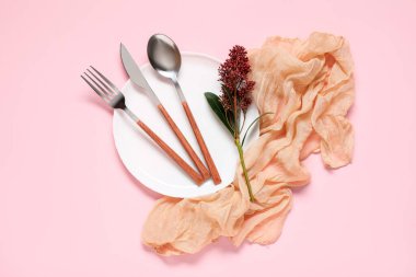 Gümüş çatal bıçak takımı, çiçek dalı ve pembe arka planda kumaş.