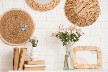 Beyaz tuğla duvarın yanındaki konsol masasında güzel çiçek buketleri olan kitaplar ve vazolar.