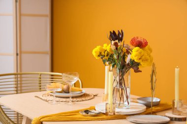 Turuncu duvarın yanında bir buket çiçek ve mum olan güzel bir masa.