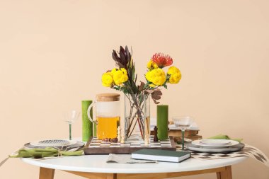 Çiçek buketi, dama tahtası ve bej duvarın yanındaki mumlarla güzel bir masa.