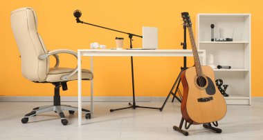 Kayıt stüdyosundaki sarı duvarın yanında dizüstü bilgisayarı ve müzik ekipmanlarıyla işyeri