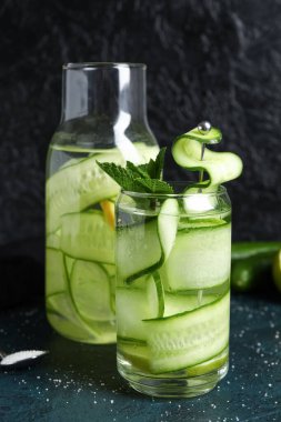 Koyu masada salatalık dilimleri ile doldurulmuş bardak ve bir şişe su.