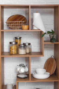 Tahta raf ünitesi, beyaz tuğla duvarın yanında kesme tahtaları ve çatal bıçakları var.