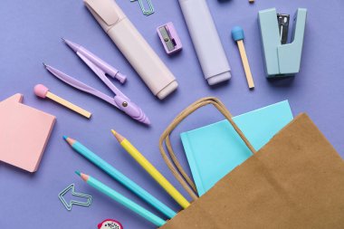 Mor arka planda farklı okul kırtasiyesine sahip alışveriş çantası.