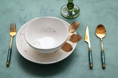 Yeşil masa üzerinde altın yapraklar ve çatal bıçak takımı olan zarif bir masa.