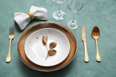 Yeşil masa üzerinde altın yapraklar ve çatal bıçak takımı olan zarif bir masa.