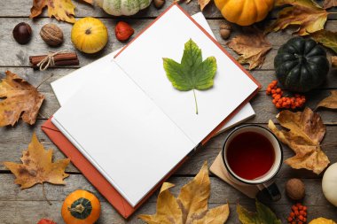 Kahverengi ahşap zemin üzerinde defter, balkabağı, çay ve sonbahar yaprakları olan kompozisyon