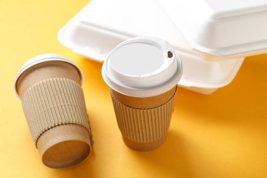Sarı arka planda paket kâğıt bardaklar ve kaplar, yakın plan.