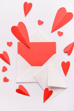 Boş kartlı zarflar ve beyaz arka planda kırmızı kağıt kalpler. Sevgililer Günü kutlaması