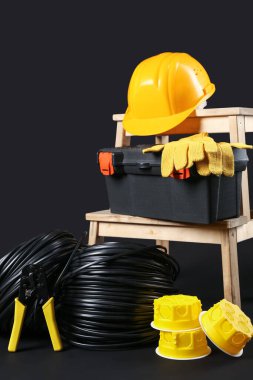 Elektrikçi aletli merdiven, rulo kablolar ve siyah arka planda sert başlık