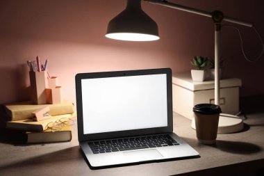 Modern dizüstü bilgisayarı, kahve fincanı, defter ve pembe duvarın yanında parlayan lamba olan bir yer.