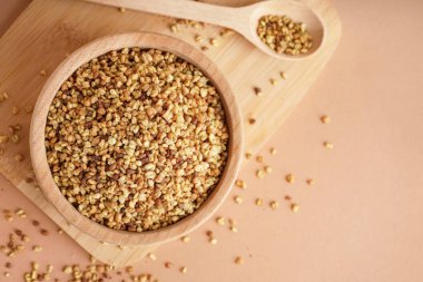 Bej arka planda çiğ karabuğday taneleri olan ahşap kase.