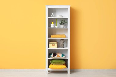 Beyaz askılar, yastıklar, mumlar ve turuncu duvarın yanında farklı dekorlar.