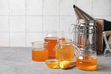 Kavanozlar, bardaklar ve bir kase tatlı bal ile gri grunge masasında Dipper.