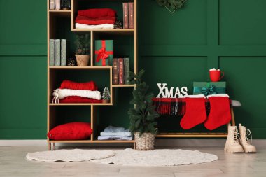 Kitaplarla dolu bir kitaplık, kışlık giysiler ve yeşil duvarın yanında Noel süsleri.