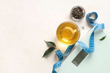 Bir fincan diyet çay, kurumuş yapraklar, mezura ve hafif arkaplanda pullar. Kilo verme konsepti