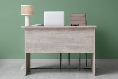 Evdeki yeşil duvarın yanındaki masa üzerinde doküman ve lamba olan modern bir laptop.