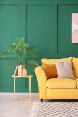 Yeşil duvarın yanında rahat sarı kanepesi ve sehpası olan şık bir oda.