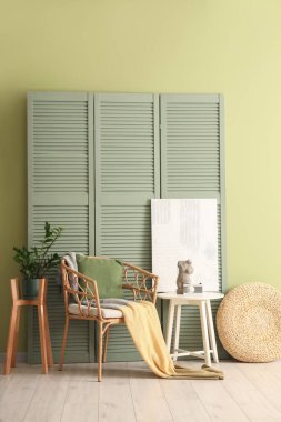 Oturma odasının içinde yeşil katlı ekran, koltuk ve masa.